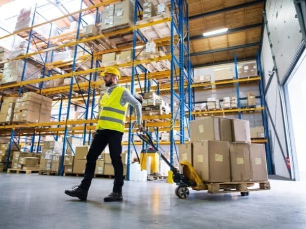 Un magazziniere trasporta scatole con un pallet manuale in un ampio magazzino magazzino conto terzi.