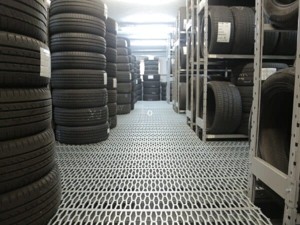Un corridoio centrale di un deposito gomme, con pile ordinate di gomme stoccate su scaffalature metalliche su entrambi i lati.