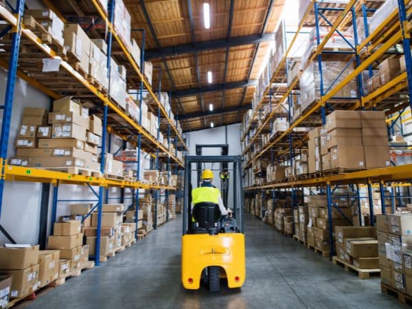Interno di un deposito merci ben organizzato con scaffalature alte piene di scatole e un operatore che guida un muletto