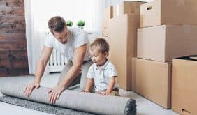 Un papà e il suo bambino stanno mettendo via un tappeto in delle scatole da trasloco