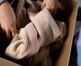 Una persona sta mettendo in una scatola da depositare un capo di abbigliamento probabilmente destinato alla donazione