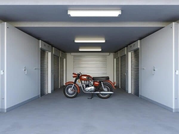 un'area di rimessaggio moto, con una moto classica parcheggiata al centro di un deposito pulito e ben illuminato, circondata da altri storage di rimessaggio individuali.
