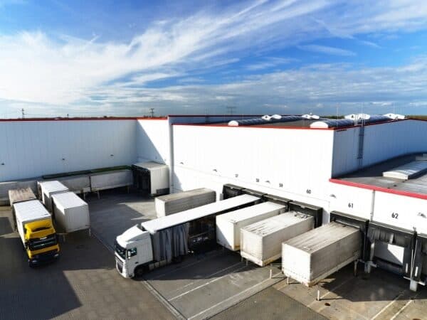 Magazzino con camion in fase di carico e scarico presso le baie di un grande deposito logistico.