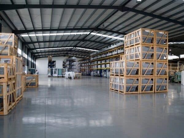 Ampio magazzino industriale con scaffali vuoti e bancali impilati in legno.